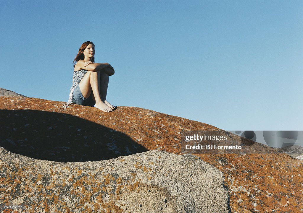 Young Woman Sits on Rock Looking at View