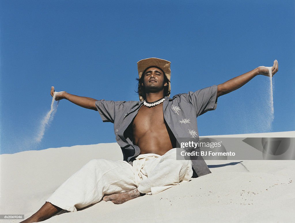 Man Wearing a Straw Hat Sits in the Sand With His Arms Out and Eyes Closed