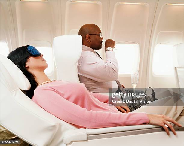 female passenger sleeping and man drinking a drink in an aircraft cabin interior - recostarse fotografías e imágenes de stock