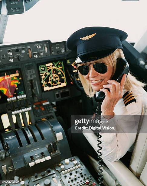 portrait of a female pilot sitting at the cockpit, talking on the phone - uniform cap imagens e fotografias de stock