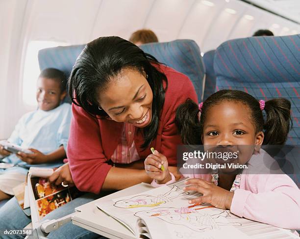 woman sits with her young daughter on a plane, watching her draw in her colouring-in book - colouring fotografías e imágenes de stock