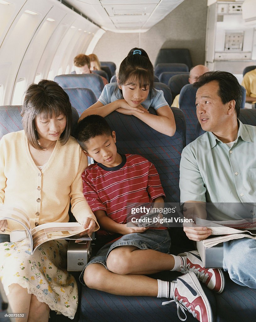 Family of Four Sit on a Plane, Reading Magazines and Playing Computer Games