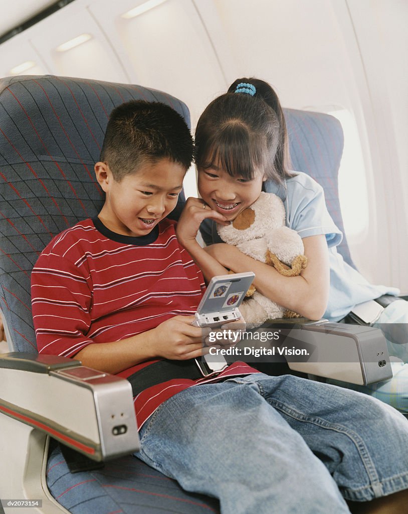Young Boy and Girl Sit on a Plane Playing a Computer Game