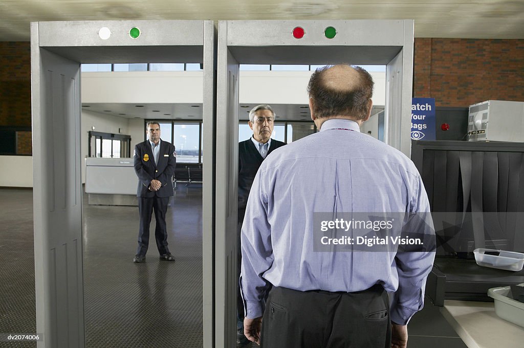 Rear View of a Balding Man Walking Through an Airport Metal Detector