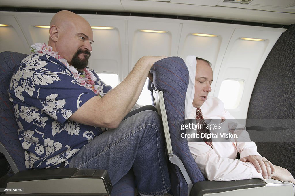 Passenger With His Knees Against a Sleeping Businessman's Chair on an Aeroplane