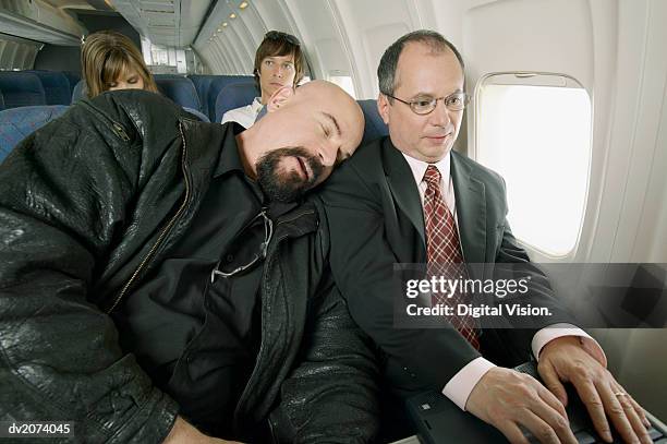 man sleeping on a plane with his head resting on a businessman's shoulder - man sleeping in plane stock pictures, royalty-free photos & images