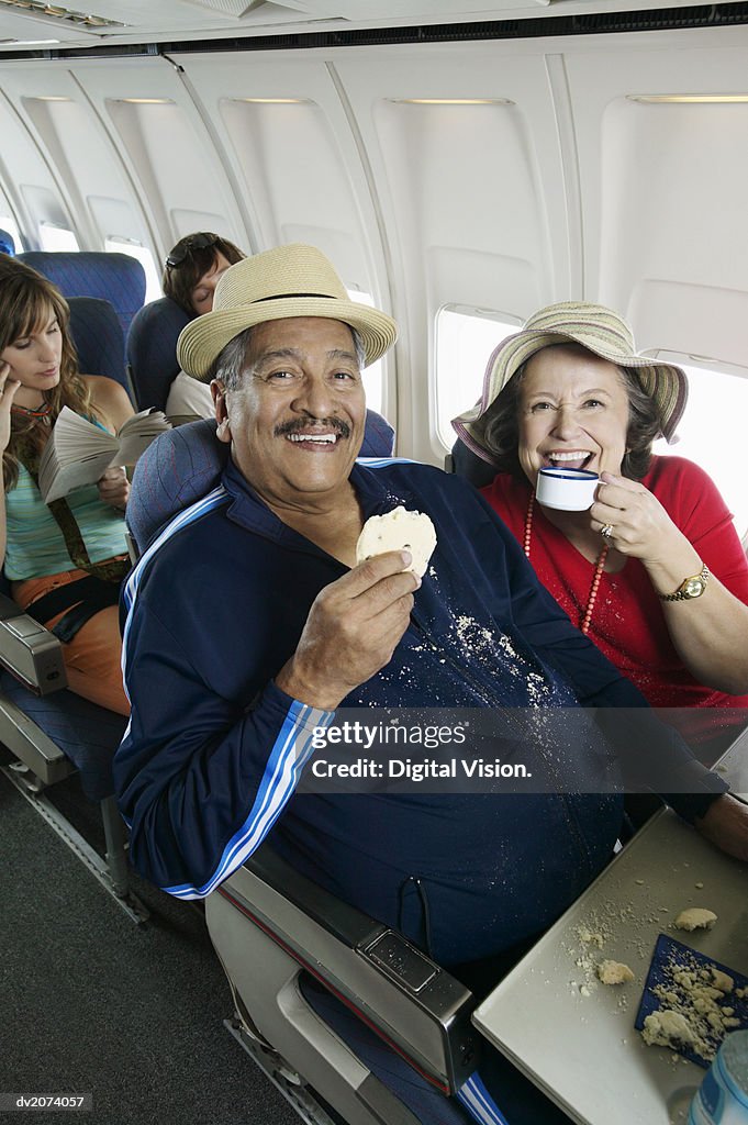 Senior Couple Sitting in an Aircraft Cabin Eating and Drinking