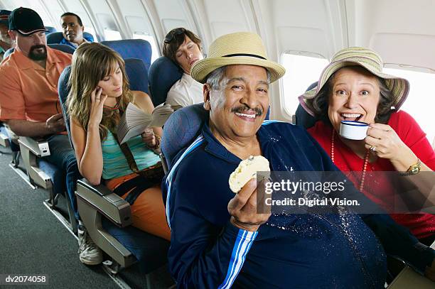 senior couple sitting in an aircraft cabin eating and drinking and passengers behind - super sensory stock pictures, royalty-free photos & images