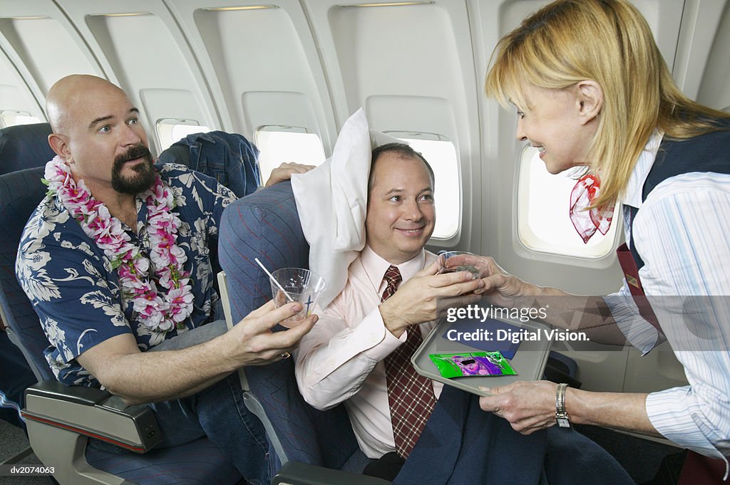Comfortable Businessman in an Aeroplane Cabin Interior Receiving a Drink From an Air Stewardess, Watched by an Annoyed Tourist