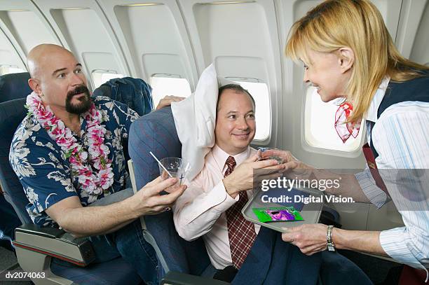 comfortable businessman in an aeroplane cabin interior receiving a drink from an air stewardess, watched by an annoyed tourist - being watched stockfoto's en -beelden