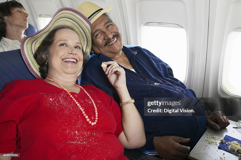 Overweight Senior Couple Sit on a Plane Sharing Cake, Crumbs on Their Clothes