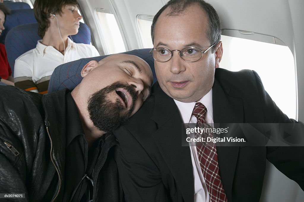 Businessman Sitting in an Aeroplane Trapped by a Man Sleeping by His Side