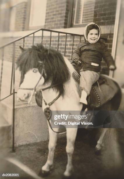 old photograph of a young girl sitting on a pony on her doorstep - zügel stock-fotos und bilder