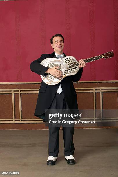 young man in an old fashioned suit stands on a stage playing a guitar - greggory stock-fotos und bilder