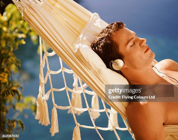 man lying in hammock listening to headphones - young man listening music and relaxing in hammock stock pictures, royalty-free photos & images