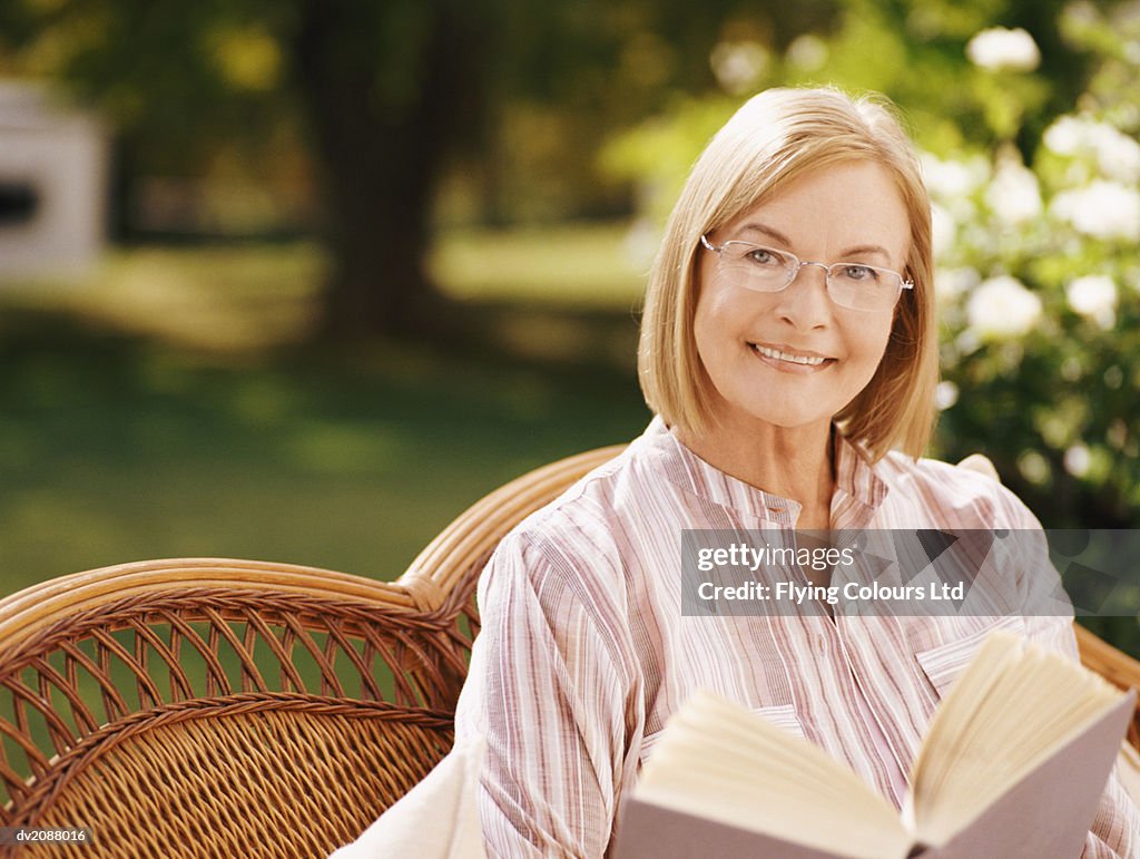 Mature Woman Sitting in a Garden Reading a Book