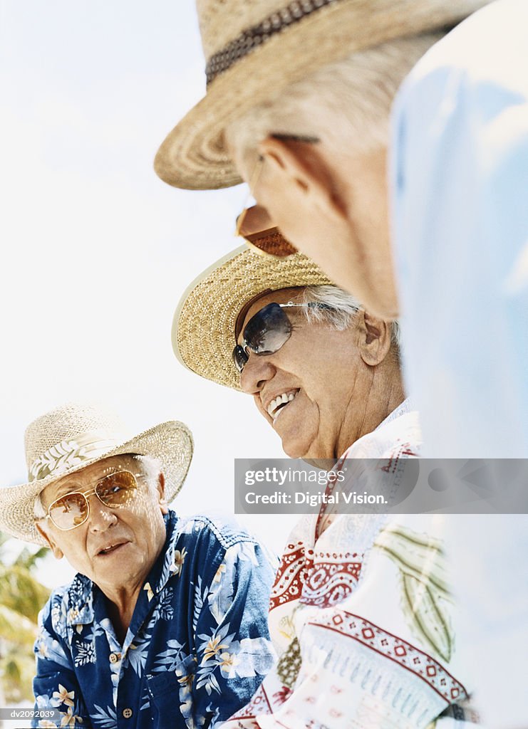 Three Senior Men in Sunhats and Sunglasses Sit Outdoors Talking