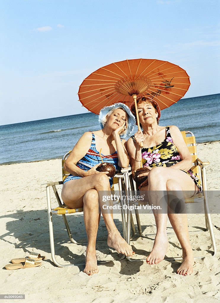 Two Bored Looking Women Sitting on Chairs Under a Parasol