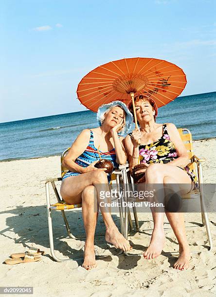 two bored looking women sitting on chairs under a parasol - coconut beach woman stock pictures, royalty-free photos & images