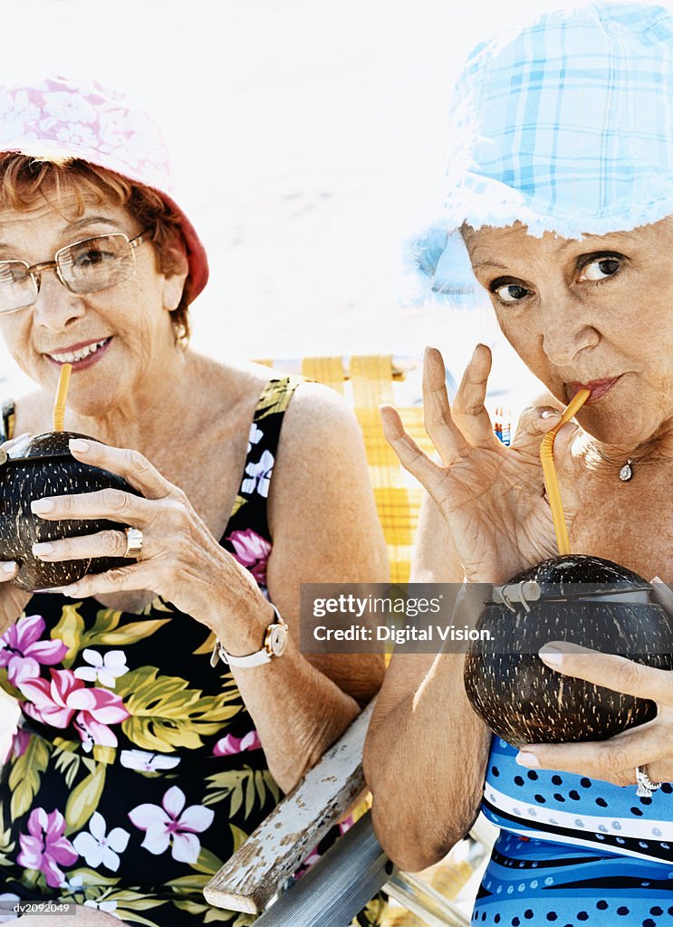 Portrait of Two Senior Women in Swimming Costumes and Sunhats Drinking Coconut Cocktails