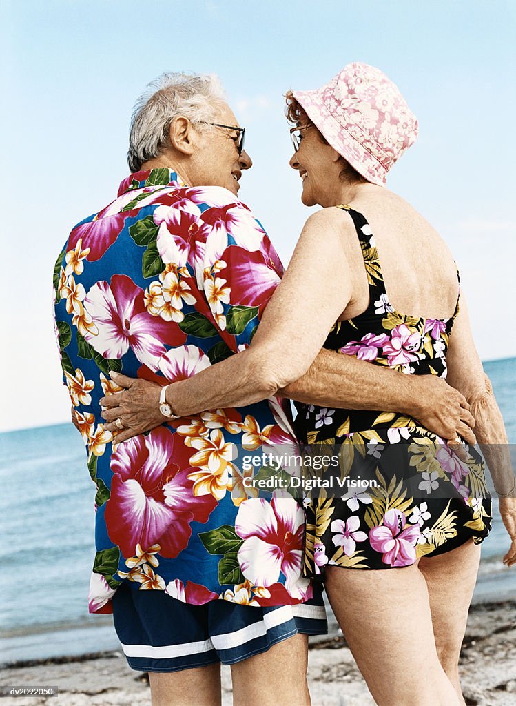 Rear View of a Senior Couple in Colourful Swimwear Standing on the Beach With Their Arms Around Each Other