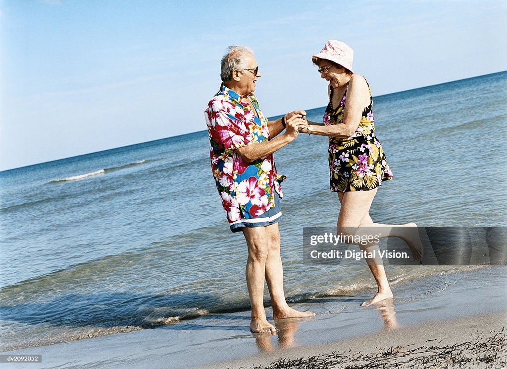 Carefree Senior Couple Dance on the Beach at the Water's Edge