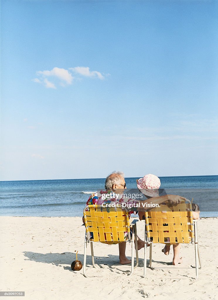 Senior Couple Sit on Deckchairs on the Beach, Talking