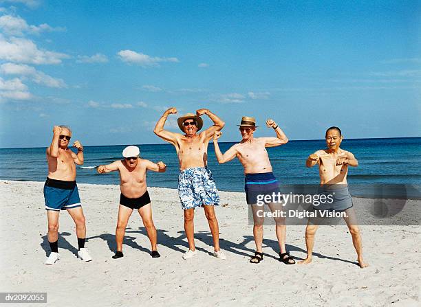 five senior men in swimming trunks stand on the beach flexing their muscles - 5 funny stockfoto's en -beelden