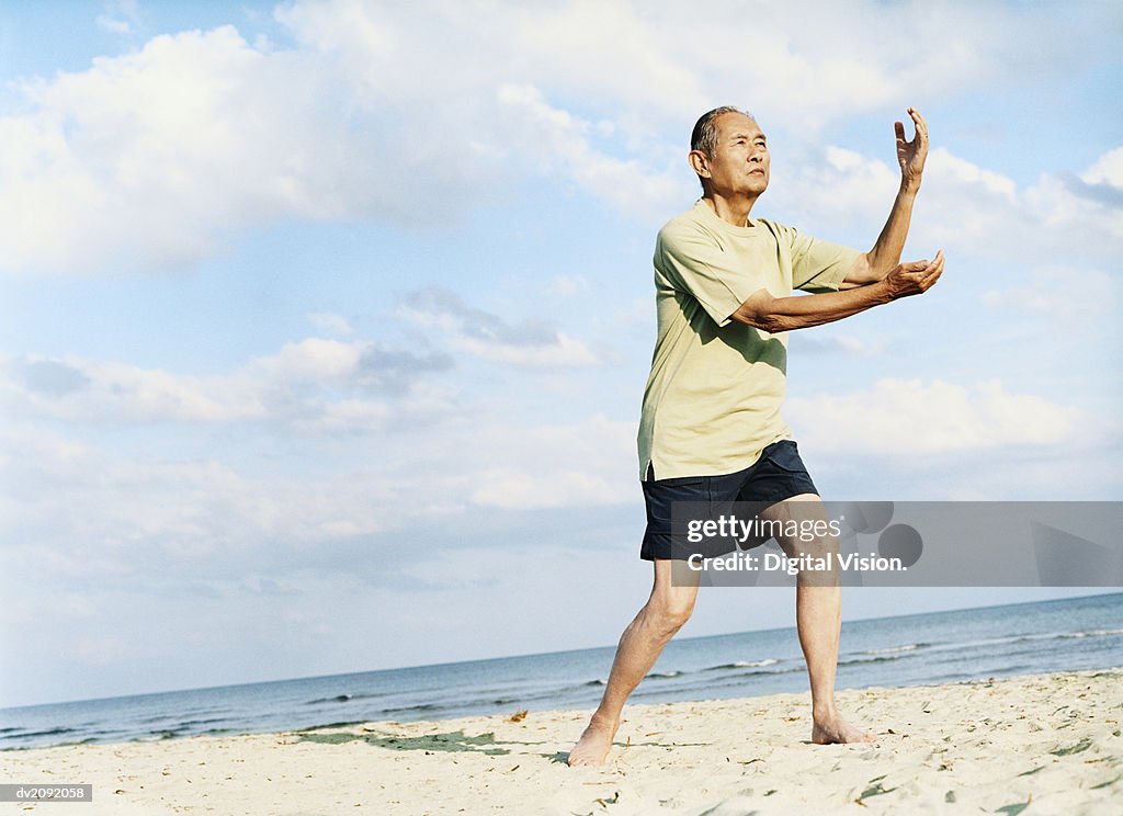 Senior Man Stands on the Beach Doing Tai Chi