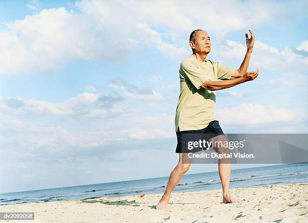 senior man stands on the beach doing tai chi - tai stock pictures, royalty-free photos & images