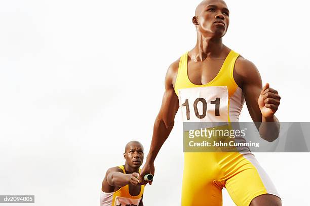 relay runner passing a baton to a determined looking team mate - sports competition format stock pictures, royalty-free photos & images