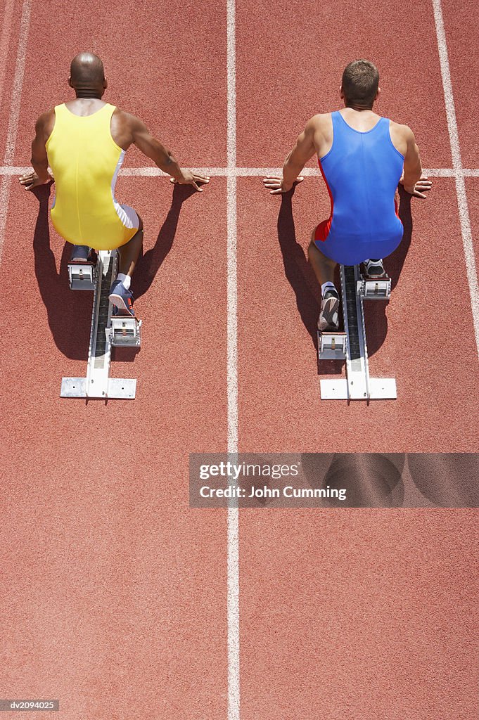 Two Crouching Athletes Lined Up on Starting Blocks on a Running Track