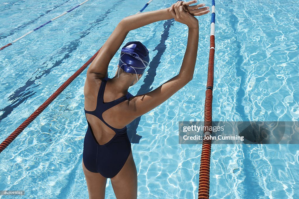 Rear View of a Female Swimmer Stretching in Front of a Swimming Pool