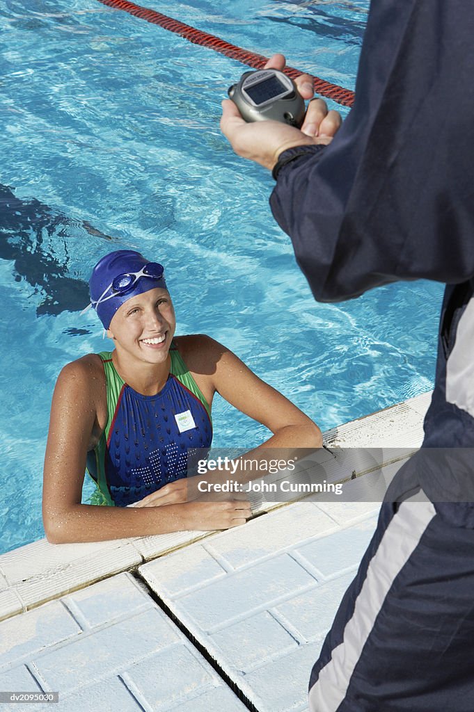 Female Swimmer at the Edge of a Swimming Pool Being Timed by Her Coach