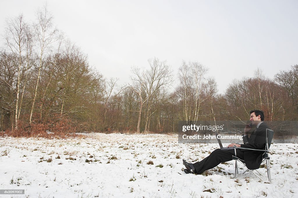 Businessman Sitting Outdoors in Snow Using a Laptop Computer