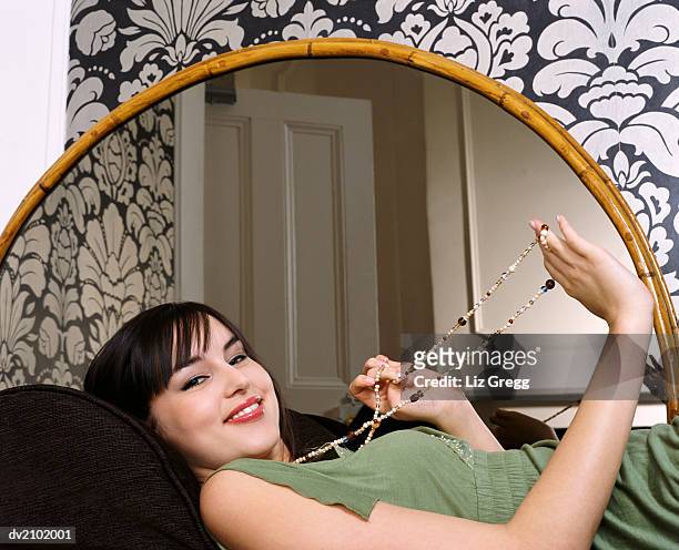 portrait of a young woman lying on a couch by a mirror, wearing a bead necklace - liz white stock pictures, royalty-free photos & images