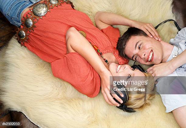 young couple lie on a fur rug listening to music on headphones - liz white stock pictures, royalty-free photos & images