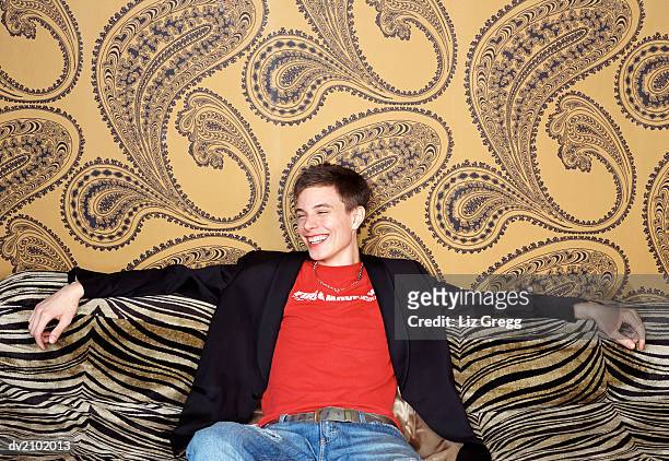 portrait of a young man sitting on a zebra print sofa, laughing - liz white stock pictures, royalty-free photos & images