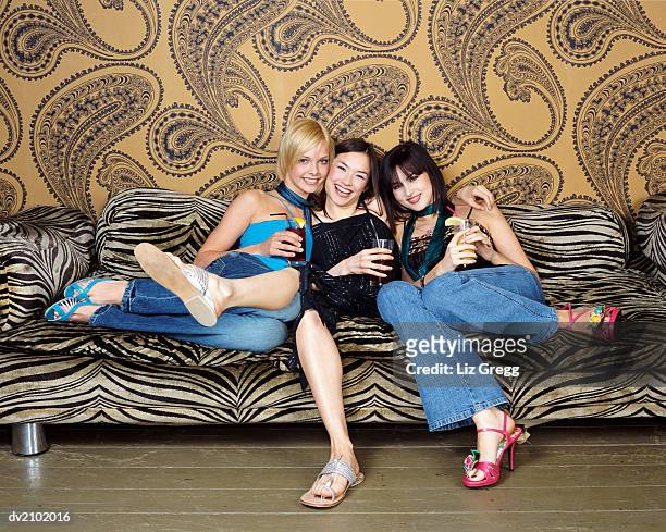 three young women sitting on a zebra print sofa holding drinks - liz white stock pictures, royalty-free photos & images