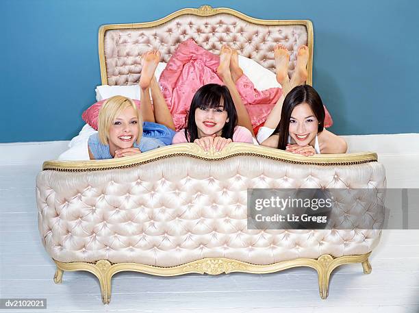portrait of three young women lying on an ornate silk bed - ornate house furniture stock-fotos und bilder