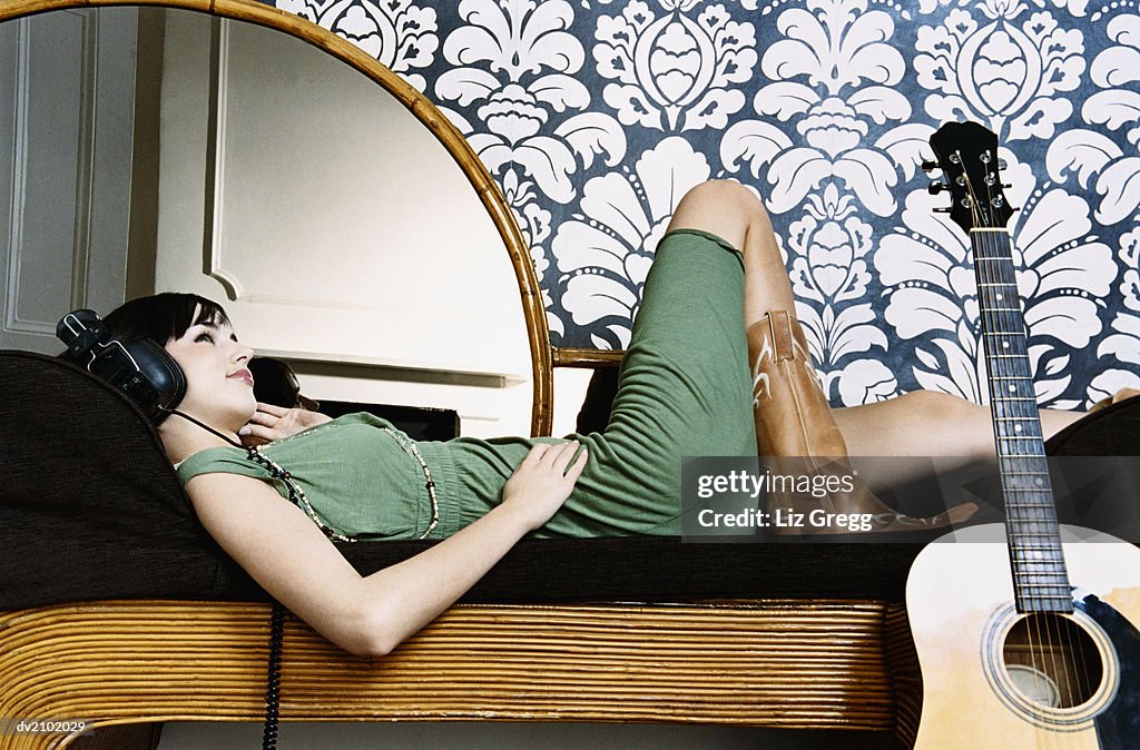 Young Woman Lying on a Chaise Lounge and Listening to Music on Headphones