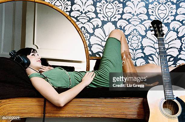 young woman lying on a chaise lounge and listening to music on headphones - liz white stock pictures, royalty-free photos & images