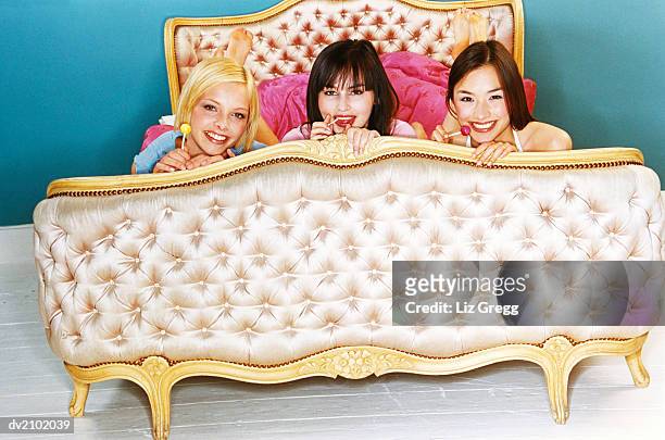 portrait of three young women on a luxurious bed - liz white stock pictures, royalty-free photos & images