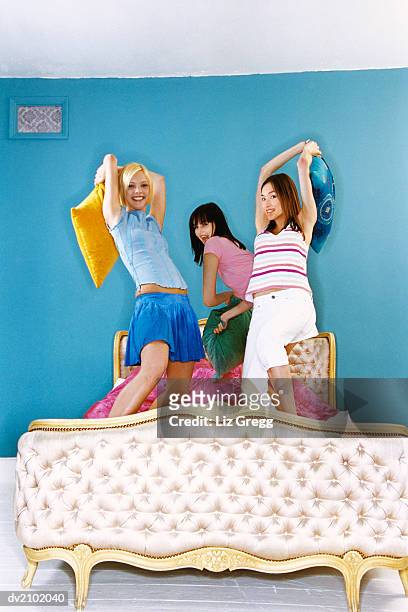 portrait of three young women having a pillow fight on a luxurious bed - liz white stock pictures, royalty-free photos & images
