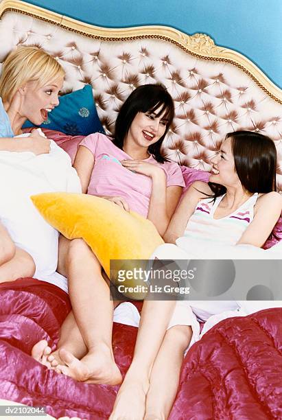 three young women lying on a luxurious bed - liz white stock pictures, royalty-free photos & images