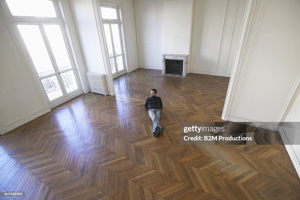 Elevated View of a Man Lying in an Empty Room with a Wooden Floor