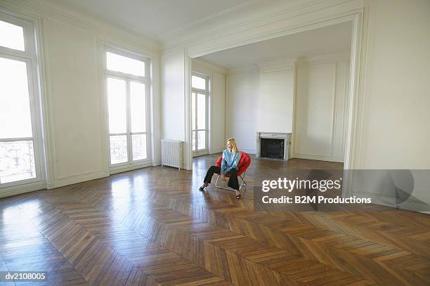 woman sitting on a red chair in a large empty room - women wearing nothing fotografías e imágenes de stock