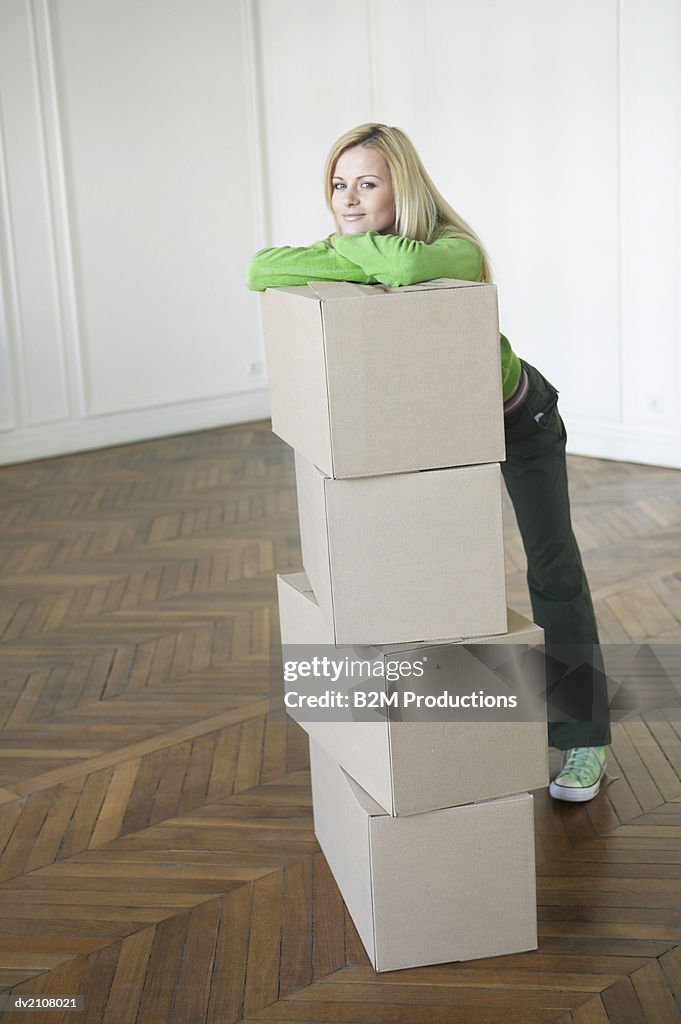 Young Woman Leaning Against a Stack of Cardboard Boxes in an Empty Room