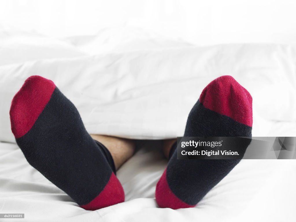 Man Wearing Socks Underneath a Duvet in Bed