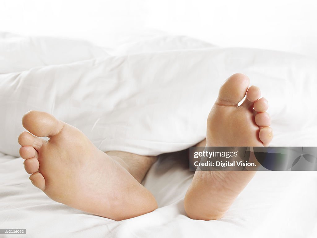 Man's Feet Underneath a Duvet in Bed